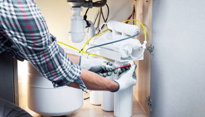 Consider installation and daily use | tycoonstory media A person working on installing a water filtration system under the sink, wearing gloves and connecting the components of the system.