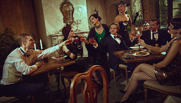 Engagement beats passive outings | tycoonstory media A group of elegantly dressed people enjoying a murder mystery dinner, raising their glasses in a festive toast while surrounded by a luxurious dining setting.