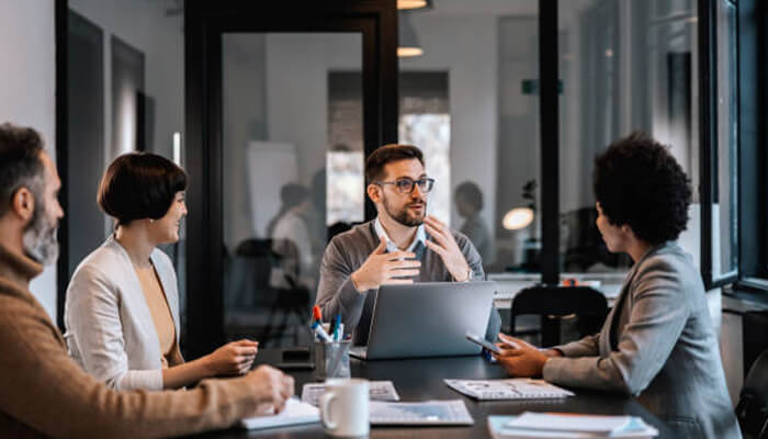 Enhancing team collaboration | tycoonstory media A business team discussing strategies in a modern office setting, with a laptop open showcasing microsoft 365 support tools to enhance team collaboration and productivity.