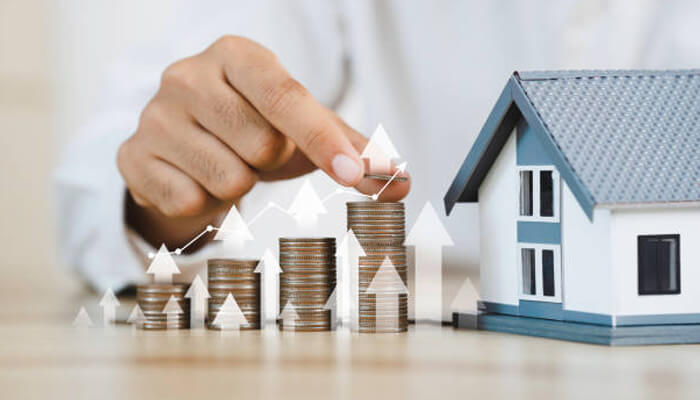 Financial benefits of proactive property management | tycoonstory media Maintaining and upgrading property is crucial for maximizing long-term financial growth, as demonstrated by the hand arranging coins next to a house model with rising arrows, symbolizing increased value and investment returns.