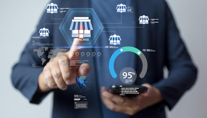 Franchise ramp | tycoonstory media A business professional using a mobile phone to analyze franchise development data, with digital charts and statistics around the concept of "franchise development marketing agencies" displayed on a virtual screen.