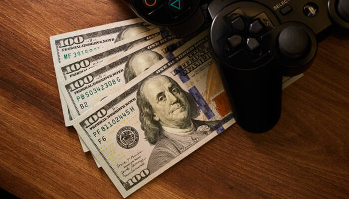 High-yield gameplay earning while doing | tycoonstory media A stack of hundred-dollar bills next to a gaming controller, symbolizing the potential earnings from mlb 26 stubs and the connection between gaming and rewards.