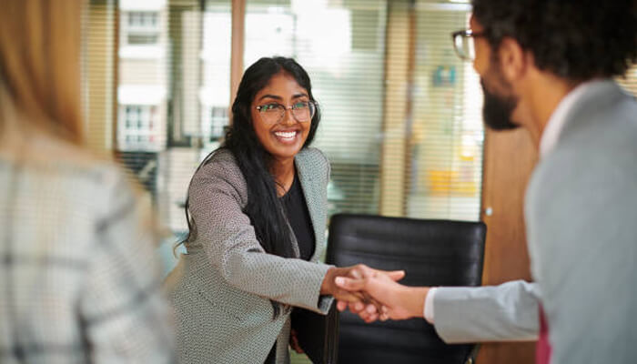 How the hiring process actually works | tycoonstory media A positive interaction between two professionals, with a lean startup team approach in mind, as they shake hands and discuss ideas in a collaborative office setting.