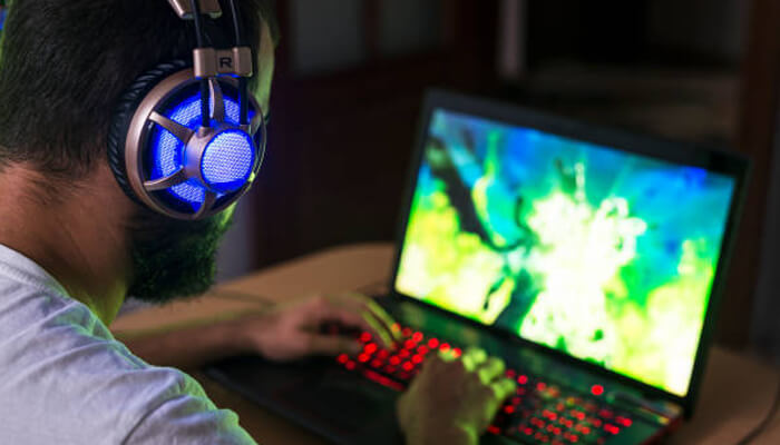 Laptops and portable pcs | tycoonstory media A gamer wearing headphones while using a laptop to play games, showcasing the immersive experience that can also be enhanced with a mobile device for playing.