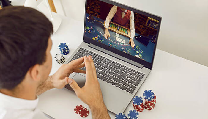 Learn the game mechanics first | tycoonstory media A person playing an online casino game on a laptop with a live dealer. Poker chips surround the laptop as the player learns the game mechanics of squeenaud.