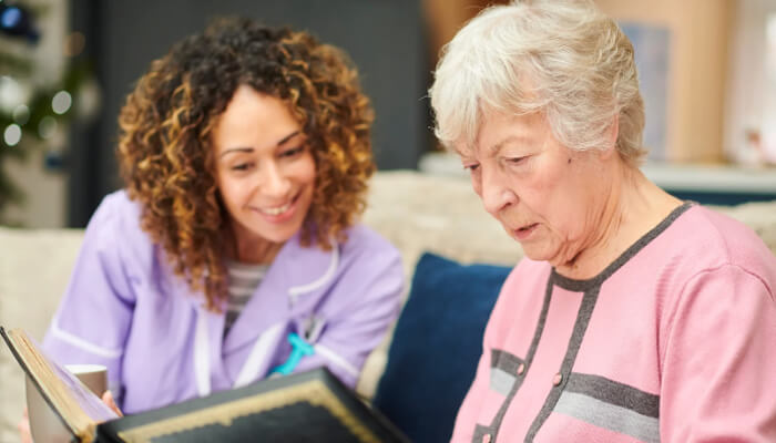 Memory care community | tycoonstory media A caregiver and a senior woman looking at a photo album together, highlighting the importance of personalized memory care in maintaining connection and well-being.