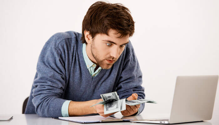 Why salary alone is no longer enough | tycoonstory media A person looking at money in front of a laptop, reflecting the importance of employee retention strategies in maintaining financial stability within a business.