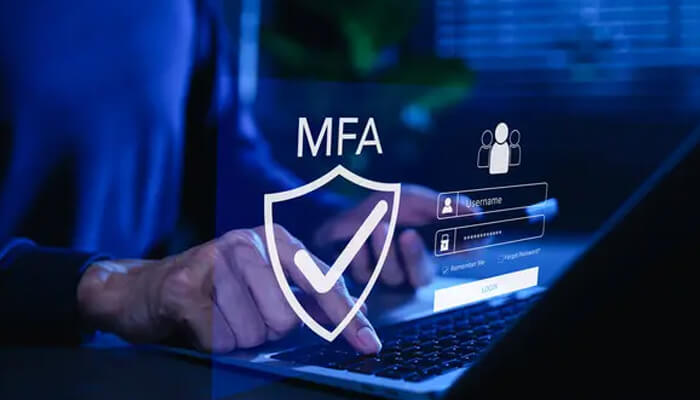 Multi-factor authentication | tycoonstory media A person enabling multi-factor authentication (mfa) on a laptop, with a shield symbol and checkmark, illustrating digital security tips for enhanced online protection.