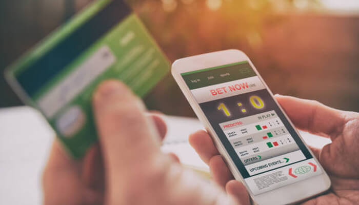 Payment options | tycoonstory media Person holding a credit card and using a mobile device to place a bet, with live score updates visible on the screen. This scene reflects the easy-to-use payment options on platforms like we88 review.
