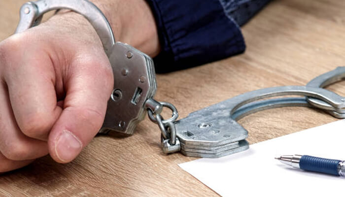 Responsibilities after release | tycoonstory media A close-up of a person’s hand in handcuffs, with a pen and paper on the desk, representing the legal process. This image highlights the role of a bail bond in securing release after an arrest.
