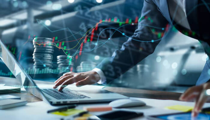 Stock market | tycoonstory media A businessman working on a laptop with financial charts and coins, symbolizing how entrepreneurs build wealth through smart investments and strategic planning.