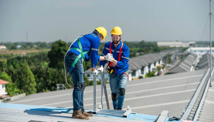 Supporting operational efficiency | tycoonstory media Two workers on a roof wearing safety harnesses and helmets, demonstrating the importance of roof safety solutions to ensure safety and compliance while working at heights.