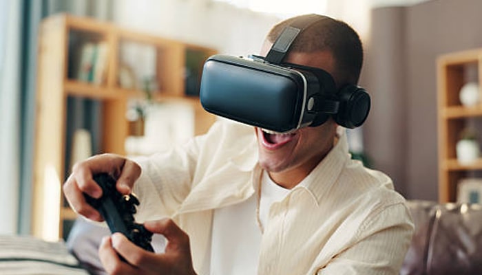 Untitled-1 | tycoonstory media Person wearing a vr headset while playing a video game with a controller, indoors and smiling with excitement.