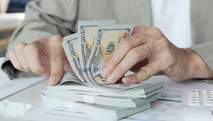 Use credit carefully during the first year | tycoonstory media Someone counting money on a desk, surrounded by paperwork and a calculator, emphasizing the need to navigate loan options to manage cash flow and financial challenges.