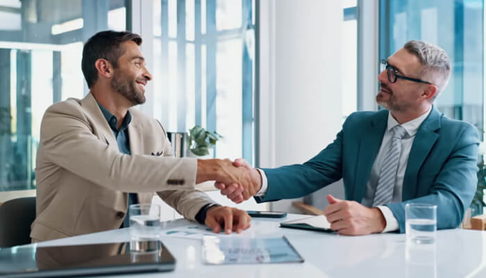 When outside thinking genuinely helps | tycoonstory media Two professionals shaking hands in an office setting, representing successful business collaboration, highlighting trust and partnership, similar to nicholas mukhtar’s approach.