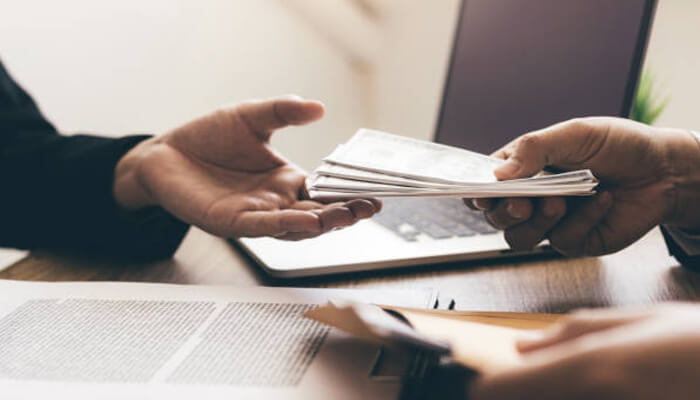 When to seek compensation and from whom | tycoonstory media A person handing over a stack of money, symbolizing compensation being exchanged in a legal case, such as seeking justice through truck accident lawyers.