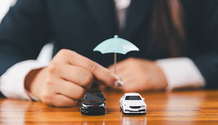 Why confusion drives skepticism | tycoonstory media A person holding an umbrella over two miniature cars, symbolizing protection in the vehicle industry. This image reflects the question of motoassure administration legit, addressing consumer concerns about vehicle protection plans. "