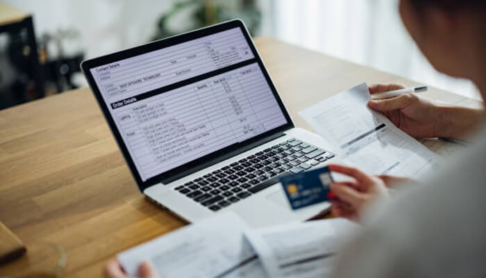 Why speed and responsibility can coexist | tycoonstory media A person is reviewing financial documents on a laptop, holding a credit card in hand. This image highlights the importance of modern lending solutions in managing finances efficiently and responsibly.