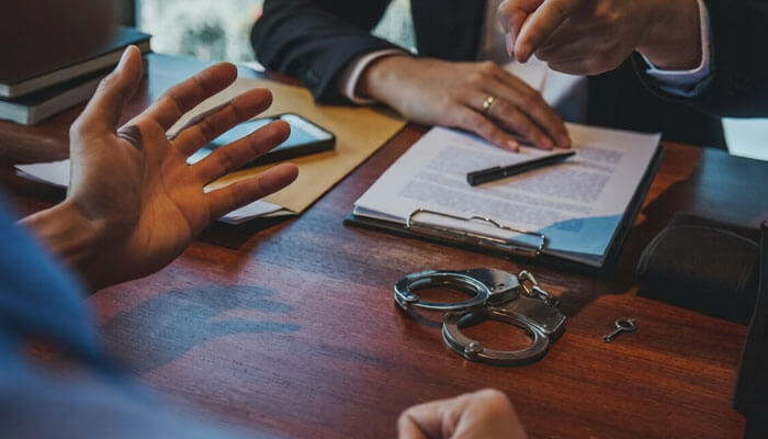 Why you need a criminal lawyer on your side | tycoonstory media A client consulting with a criminal lawyer about their case, with handcuffs on the table, highlighting the importance of legal guidance during criminal proceedings.