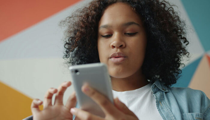 E-commerce website | tycoonstory media Young person with curly hair looking at a smartphone indoors, against a colorful geometric wall.