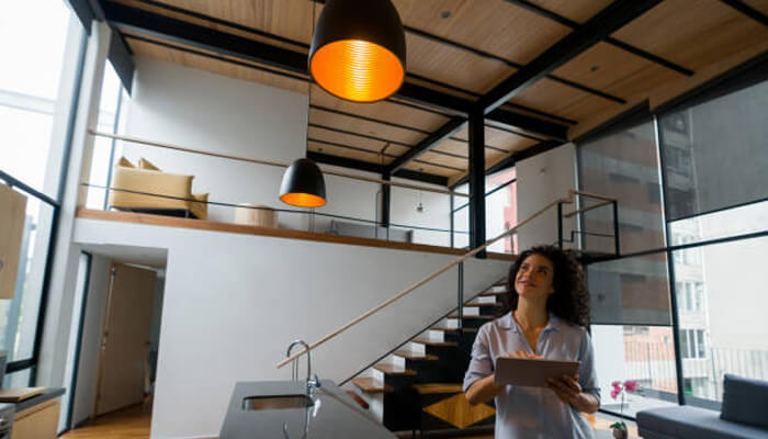 Energy management without sacrificing comfort | tycoonstory media A woman using a tablet to control lighting in a modern home, showcasing the ease and convenience of lutron solutions for automated lighting control.