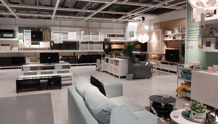 Few | tycoonstory media Bright furniture showroom with living room setups: light blue sofa, coffee tables, shelves, and tvs on display under a ceiling with exposed fixtures.