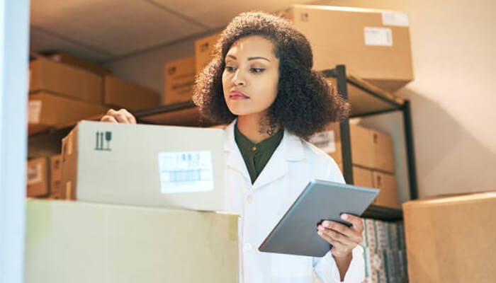 From discovery to clinical manufacturing | tycoonstory media A professional inspecting packages in a warehouse, showcasing the logistical role of drug delivery companies in ensuring accurate inventory management.