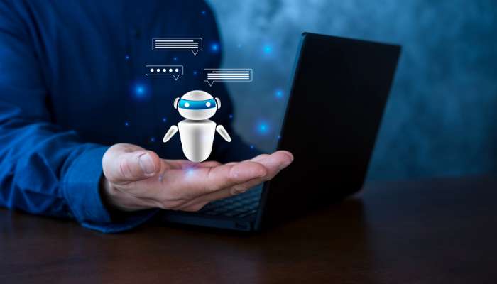 Ai voice agents for customer support automation | tycoonstory media Robot chatbot hovering above an outstretched hand beside a laptop, with chat bubbles around it.