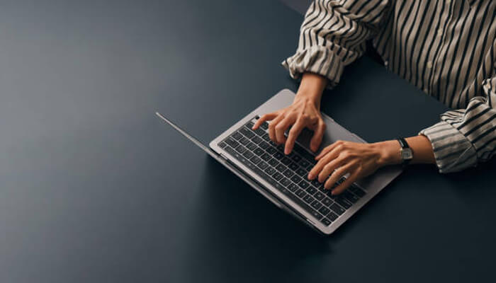 Bail applications | tycoonstory media Person typing on a silver laptop at a dark desk, wearing a striped shirt.