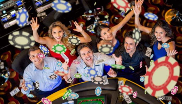 Casino | tycoonstory media A group of smiling people at a casino table throwing colorful poker chips into the air.