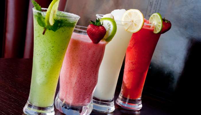 Compliance with standardized thickness levels | tycoonstory media Four tall glasses of colorful smoothies on a dark bar, garnished with mint, lime, strawberry, lemon slices (green, pink, white, red).