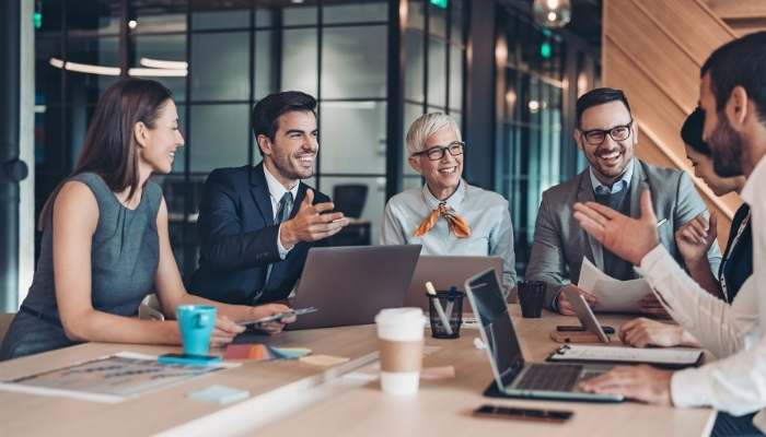 How to position your career for executive leadership roles in southeast asia 1 | tycoonstory media Five colleagues in a modern office around a conference table, sharing ideas with laptops, papers, and coffee.