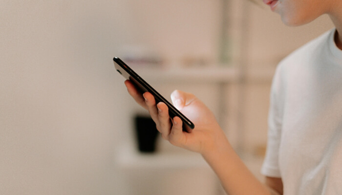 Online bail | tycoonstory media Person holding a smartphone in one hand, looking at the screen indoors.