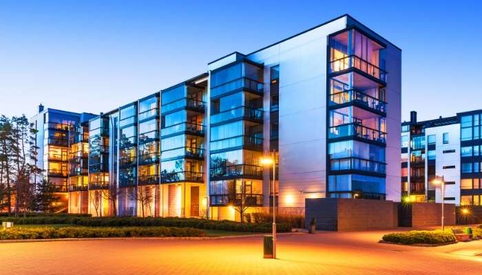 Prestige property to elevate their lifestyle and wealth | tycoonstory media Modern apartment complex at dusk with glass facades, warm interior lights, and well-lit entrance.