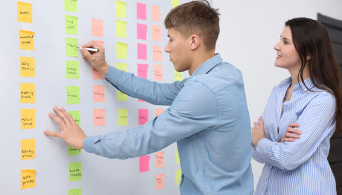 Start small and test - tycoonstory | tycoonstory media Business guide disbusinessfied: using the'Start Small and Test' strategy in business planning. Entrepreneurs and business leaders work together, brainstorming and organizing ideas with sticky notes, showcasing an iterative approach to testing and refining business strategies.