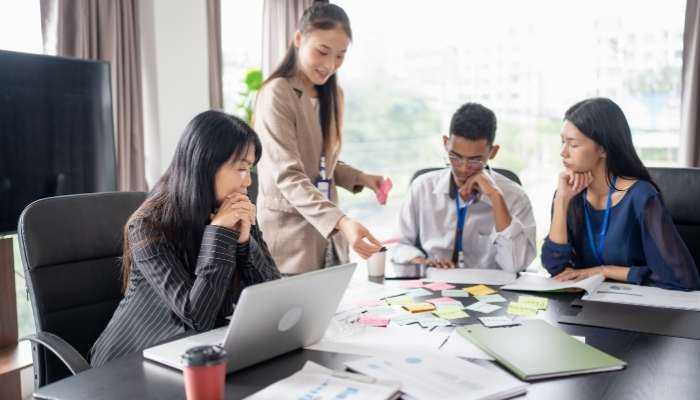 The hidden cost of interactive features | tycoonstory media Team of four professionals collaborating around a table with a laptop, sticky notes, and documents on the table