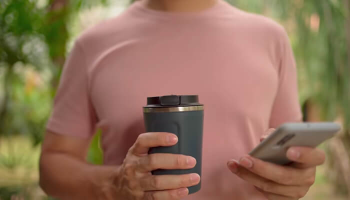 What modern corporate drinkware programs actually look like | tycoonstory media A person holding a branded tumbler and a smartphone, showcasing the convenience and appeal of customized drinkware in daily life.