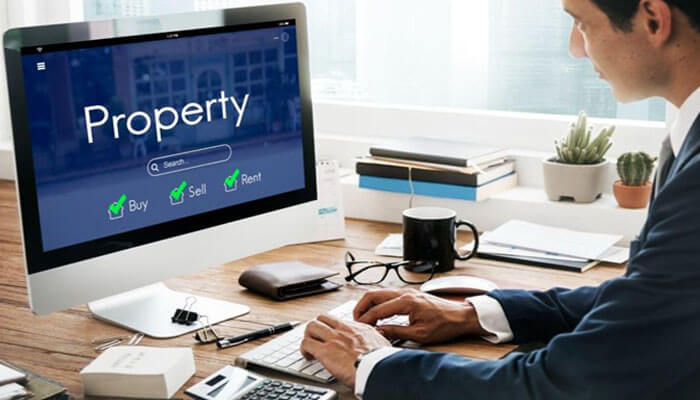 Why smart electrical systems matter for commercial property management | tycoonstory media Person at a desk using a computer displaying a real estate site titled 'property' with buy, sell, rent options