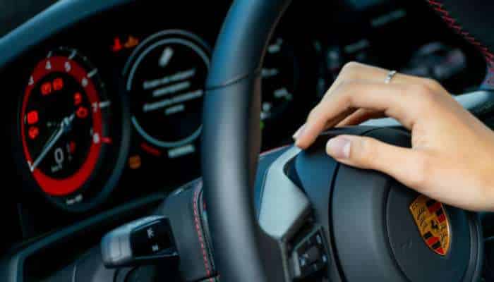 4 expert strategies for avoiding transmission failure in porsche | tycoonstory media Close-up of a driver's hand gripping a porsche steering wheel, with illuminated red and blue dashboard gauges in the background.