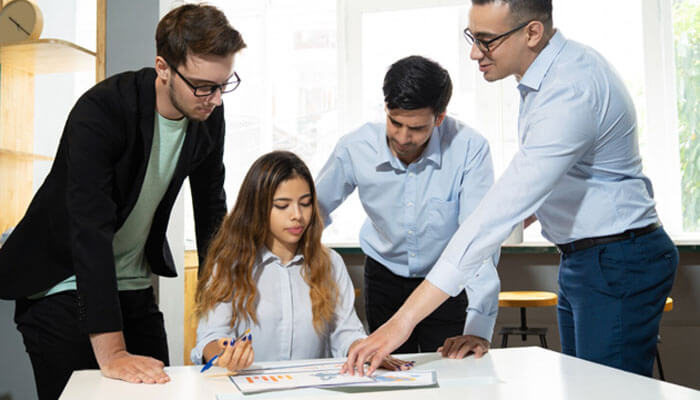 7 simple tips to ensure your employees see they are valued in your organisation - tycoonstory | tycoonstory media Four coworkers in an office gathered around a table, examining a chart on a document.