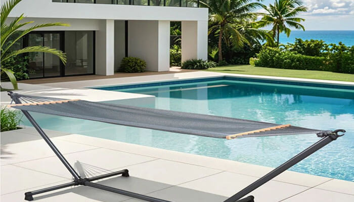 A hammock with stand - tycoonstory | tycoonstory media Modern villa with a rectangular pool and a freestanding hammock in the foreground, overlooking tropical landscaping and the ocean beyond.