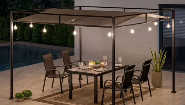 A set of string lights - tycoonstory | tycoonstory media Outdoor dining area under a pergola with string lights, six chairs, and a table set for dinner by a poolside patio at dusk/light evening glow with plants nearby.