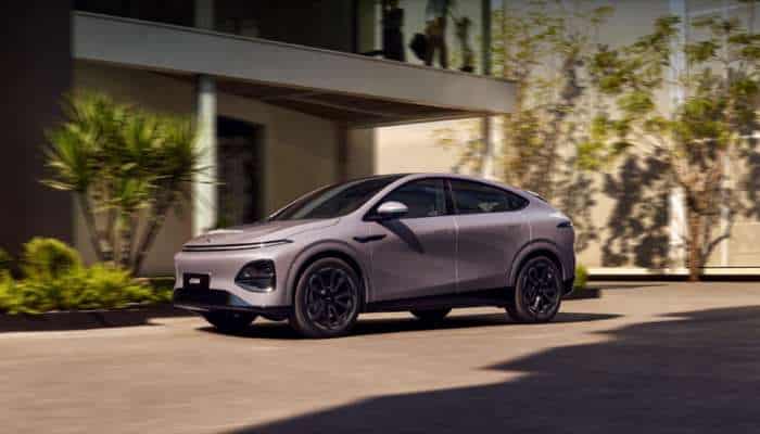 Best chinese electric cars in europe 2026 1 | tycoonstory media A metallic gray crossover suv parked on a driveway in front of a modern building with trees and shrubs nearby.