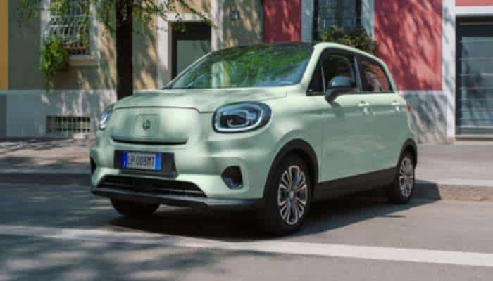 Best chinese electric cars in europe 2026 4 | tycoonstory media Mint-green compact electric car parked on a sunlit city street with colorful buildings in the background.