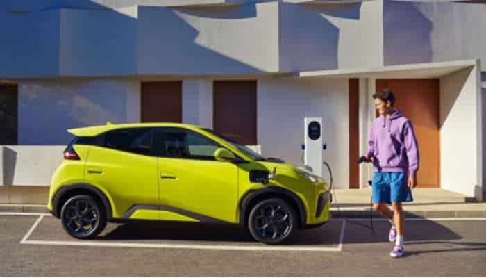 Best chinese electric cars in europe 2026 8 | tycoonstory media Bright yellow-green electric suv being charged at a parking lot as a man in a purple hoodie plugs in the charging cable.