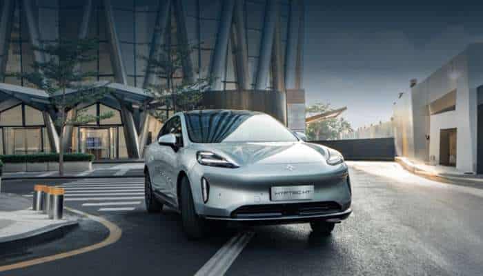 Best chinese electric cars in europe 2026 9 | tycoonstory media Silver electric suv driving on a city street in front of a modern glass building.