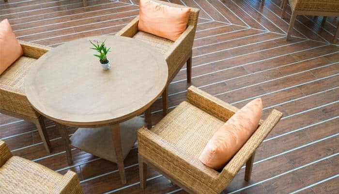 Choose weather-resistant materials - tycoonstory | tycoonstory media Round wooden table surrounded by wicker chairs with orange cushions on a wooden deck, a small potted plant in the center.