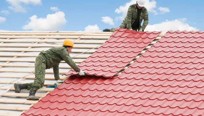 Choosing the right roofing materials - tycoonstory | tycoonstory media Twin cities roofing contractor workers installing red metal roofing sheets on a residential structure, demonstrating professional roof replacement techniques, proper underlayment alignment, and weather-resistant roofing practices designed to withstand harsh minnesota climate conditions including heavy snow, wind, and seasonal temperature shifts.