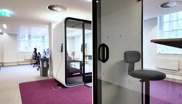 Dd | tycoonstory media Open office with a glass-walled private pod, purple carpet, and desks in the background.
