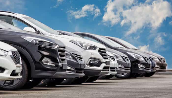 Why some cars last forever - and others don’t: can the industry change? | tycoonstory media Row of modern cars lined up in a dealership-style display under a clear sky, representing differences in automotive design philosophy and long-term durability trends in cars.